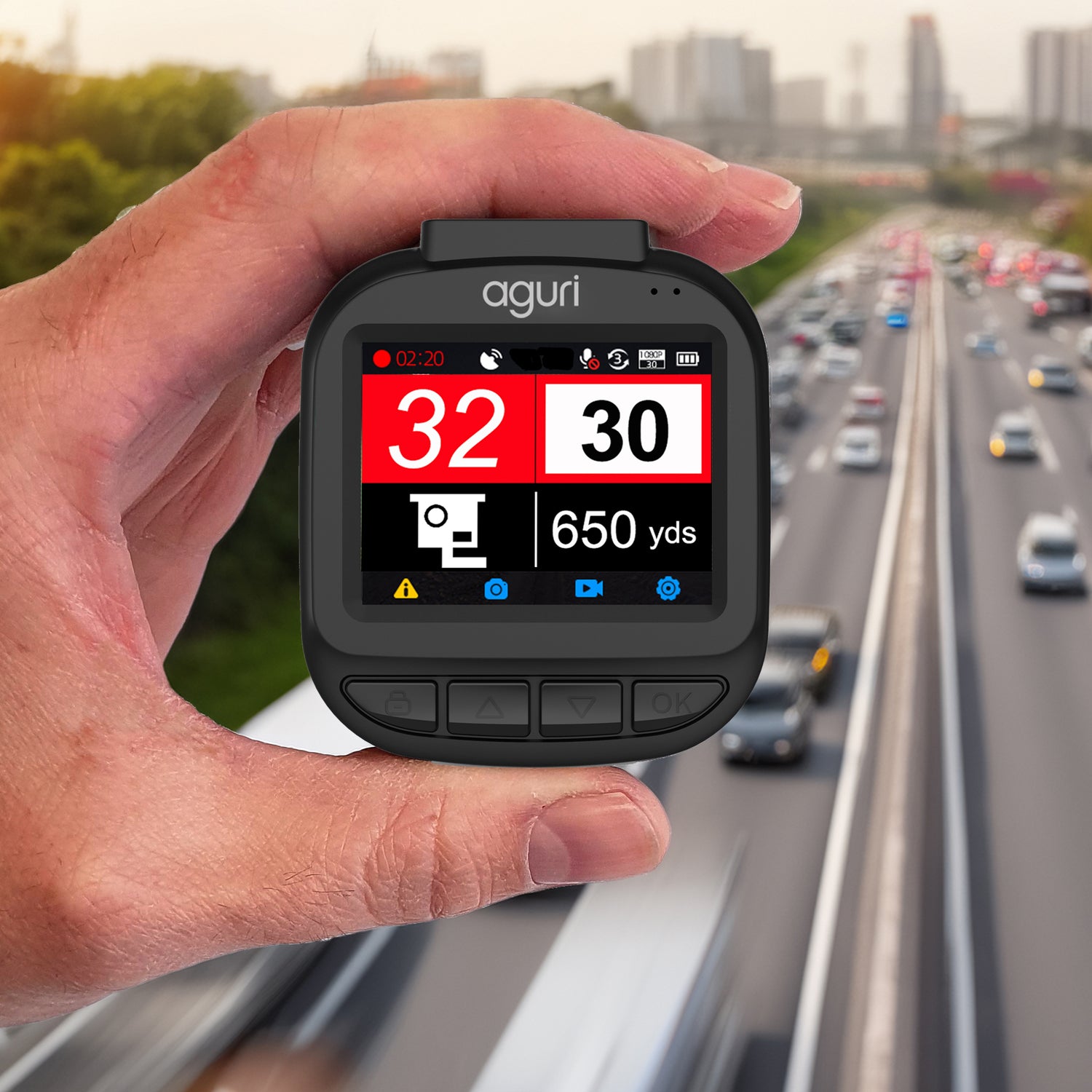Hand holding an aguri DX1250 dash cam and speed camera detector on a highway with traffic in the background